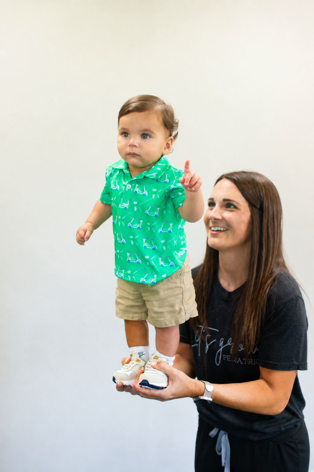 A therapist kneeling beside a young child who is standing confidently during a therapy session.