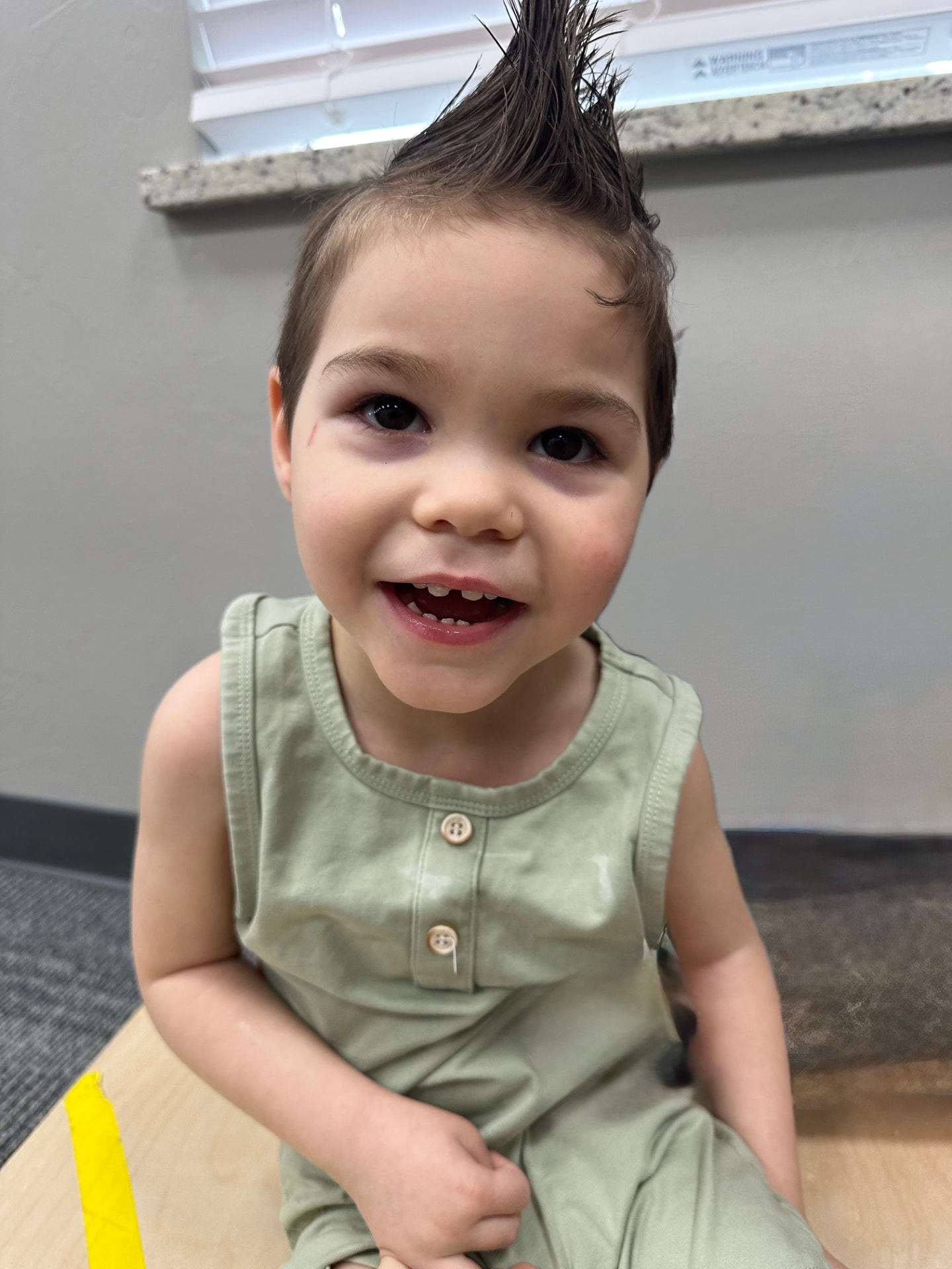 A smiling young boy with a mohawk seated during a therapy session.