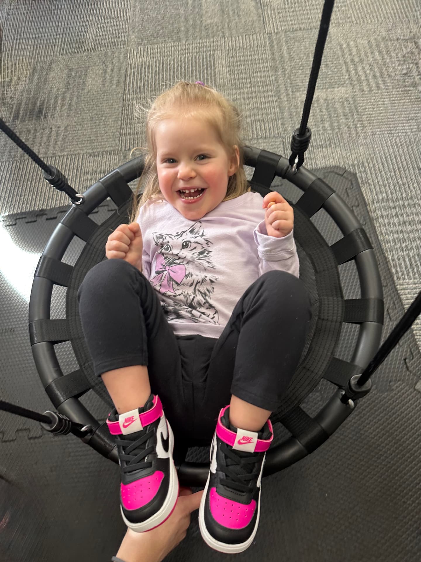 A young girl laughing while sitting in a round therapy swing.