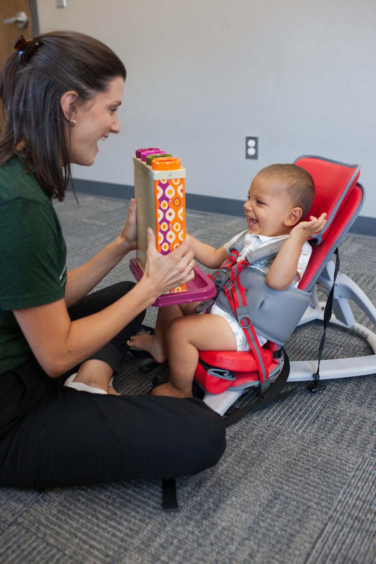 A pediatric occupational therapist working with a young boy seated in a supportive chair during a sensory integration activity.