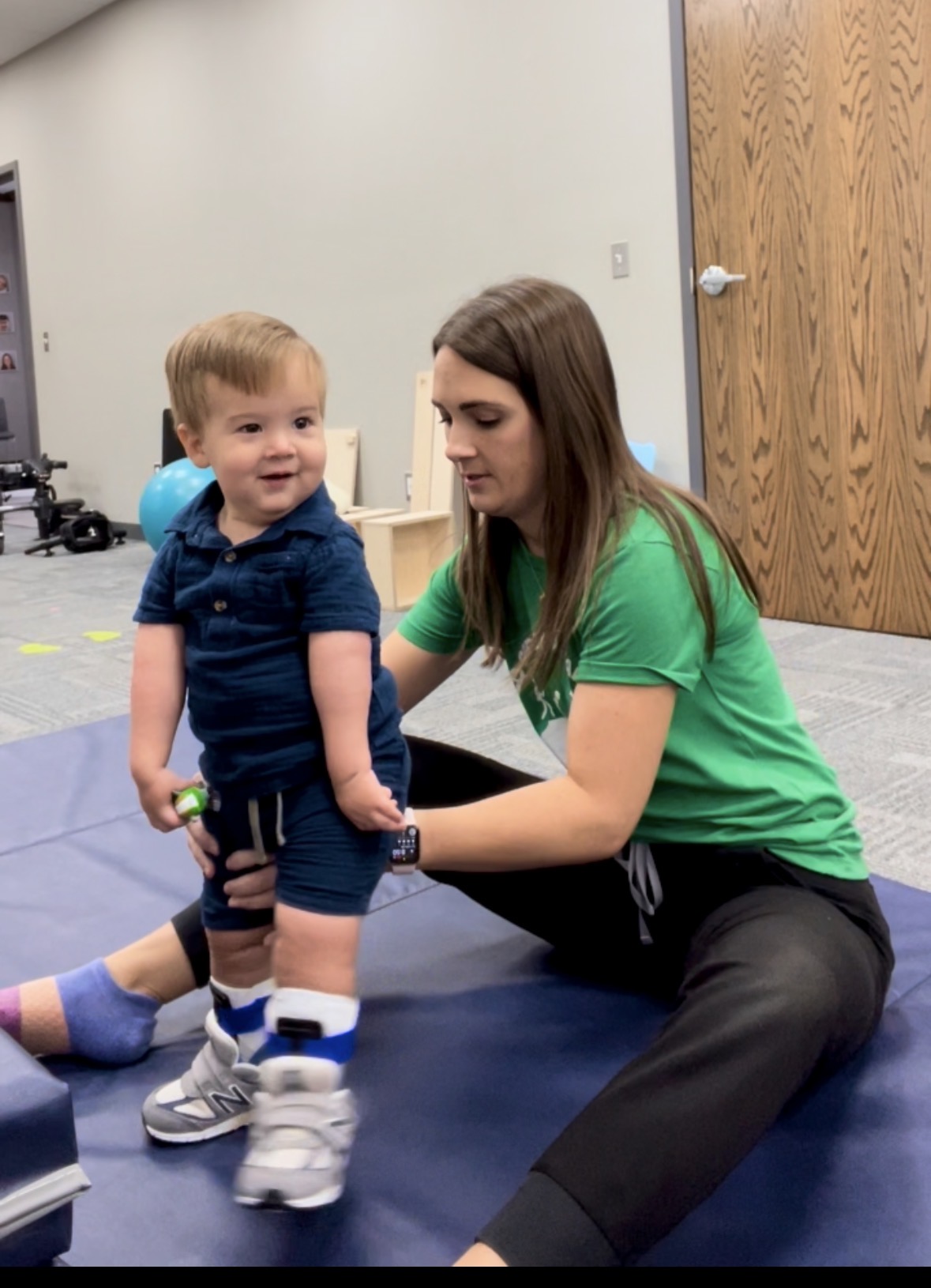 Luke standing with support from his therapist.