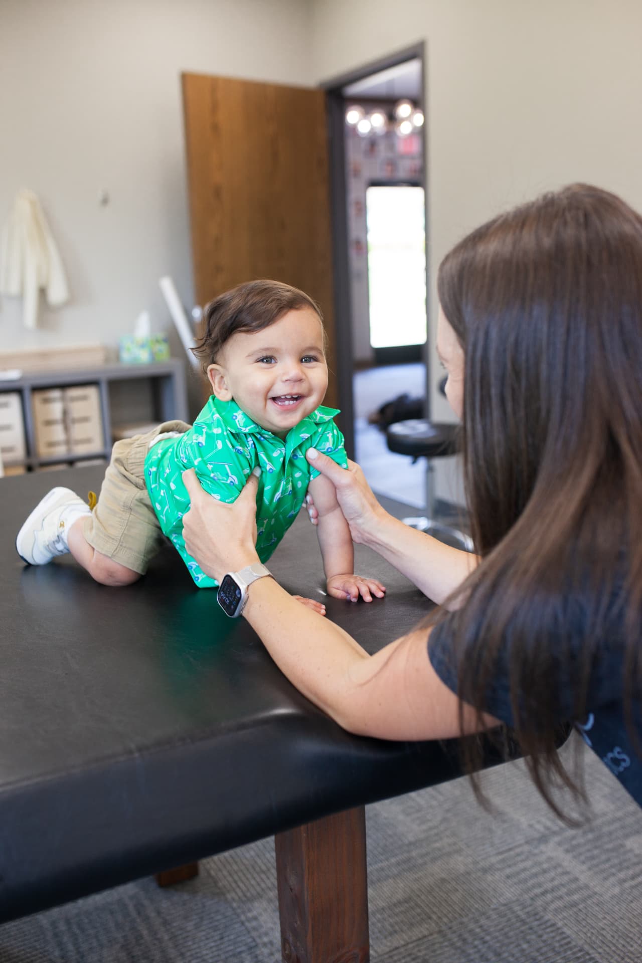 A smiling baby on the treatment mat making eye contact with pediatric physical therapist Sarah during a therapy session.