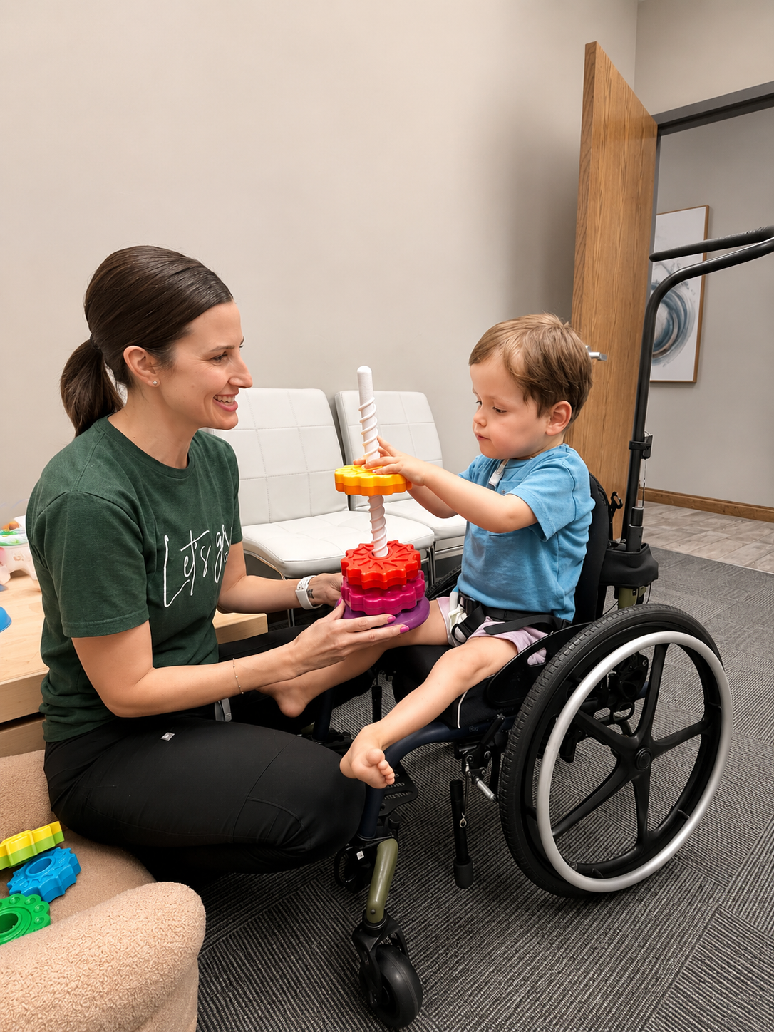 A therapist and a young boy in a wheelchair smiling together while stacking colorful rings