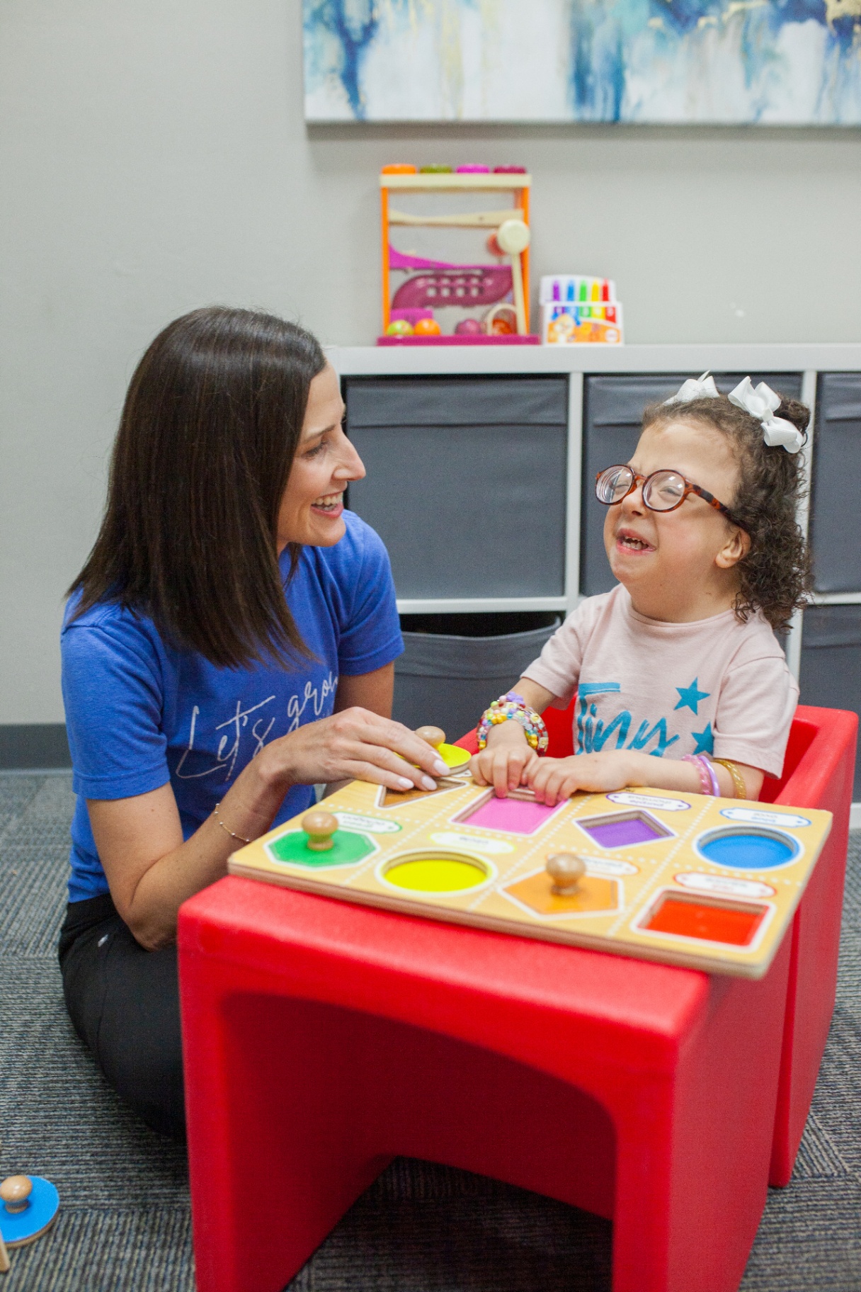 A young child working with a therapist on a fine motor activity with wooden blocks at a sunny table.