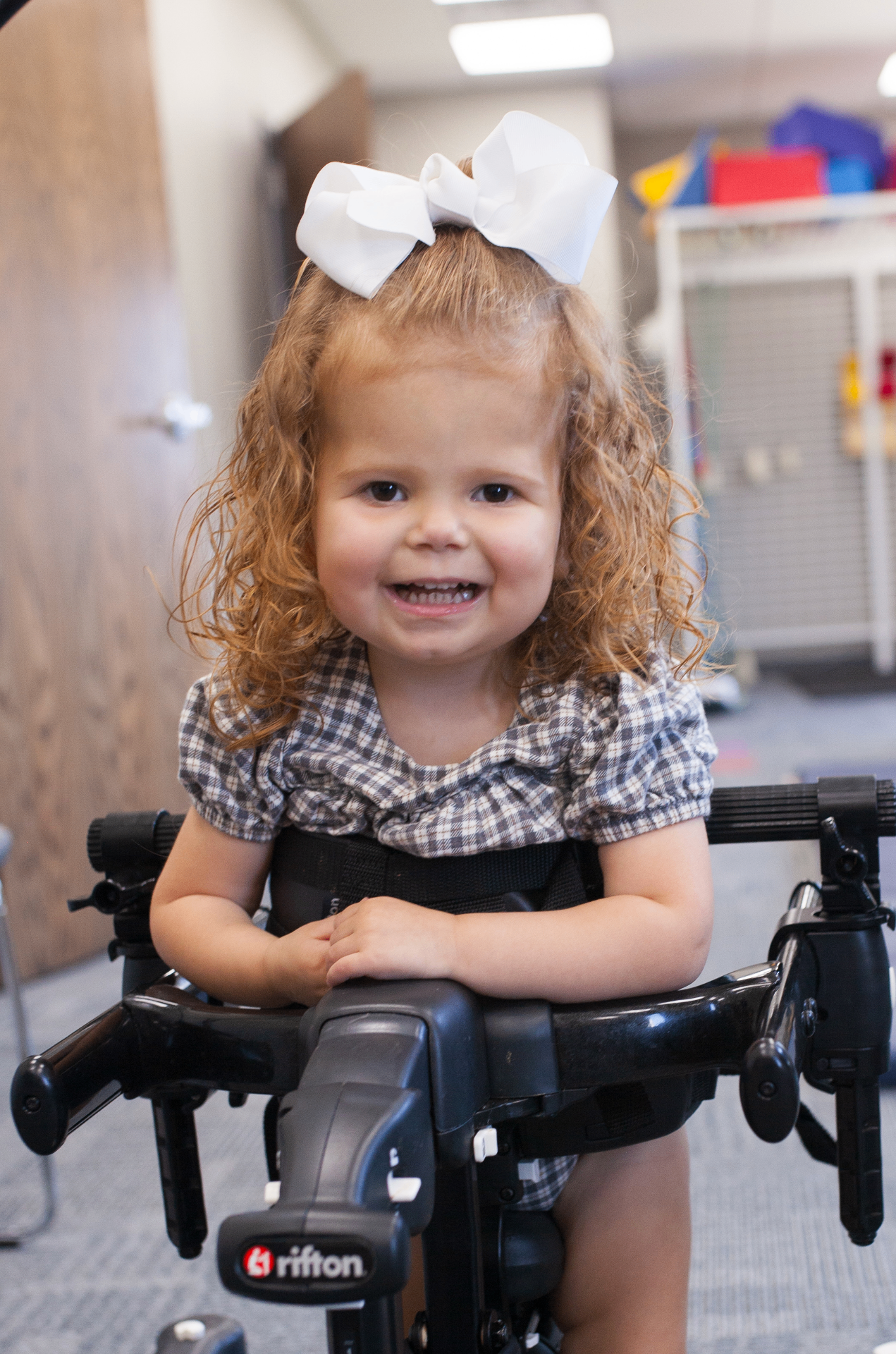Eliza smiling while using a Rifton gait trainer in the therapy gym