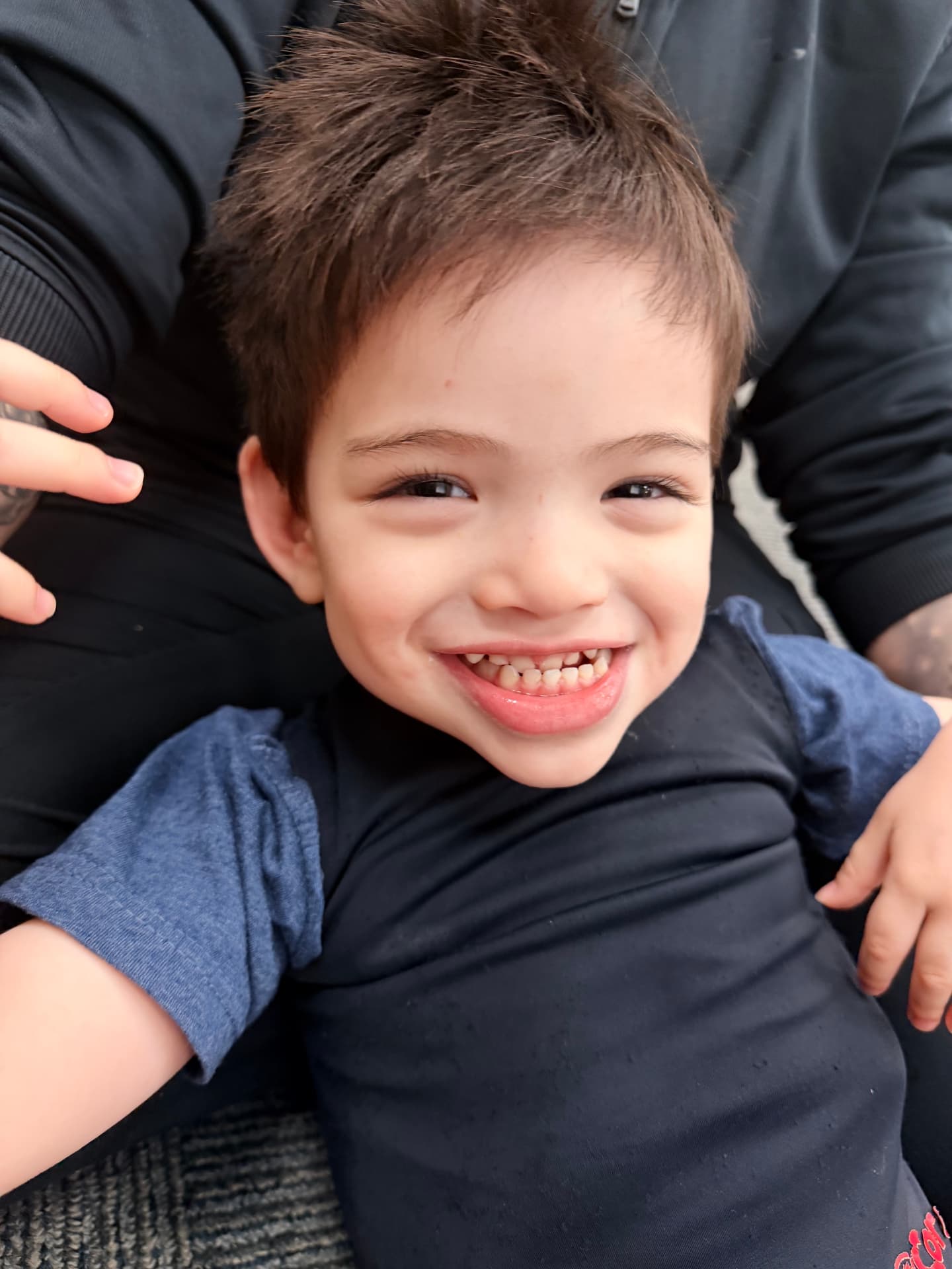 A smiling young boy with a mohawk held by a caregiver during a therapy session.